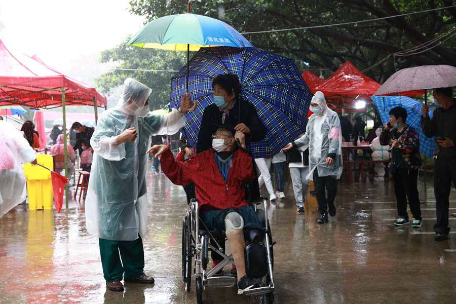 核酸采样现场，突然下起暴雨，志愿者第一时间冲上前去为市民撑伞。张长征摄
