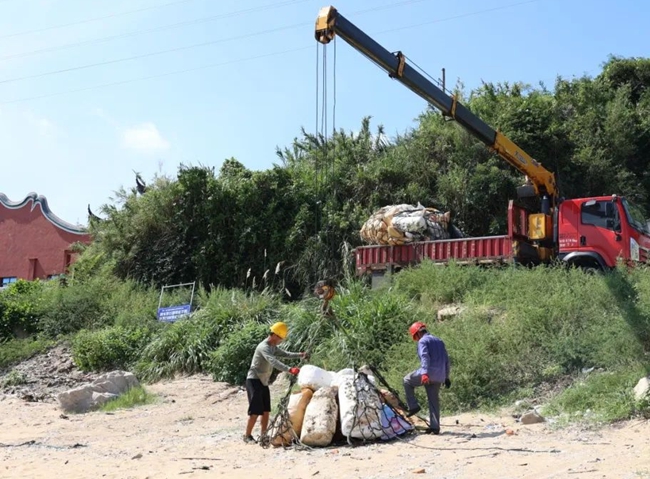 在大建村海岸沿线，环卫工人正在将垃圾打包上环卫车。