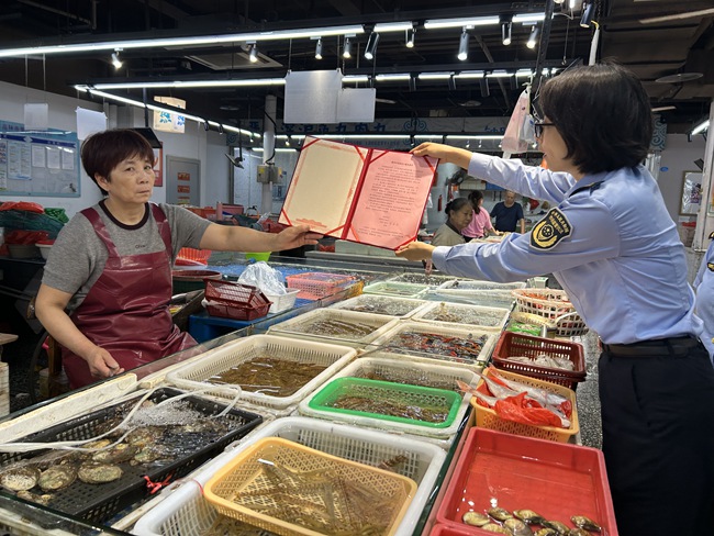 工作人员向商家介绍《水产市场诚信计量管理规范》